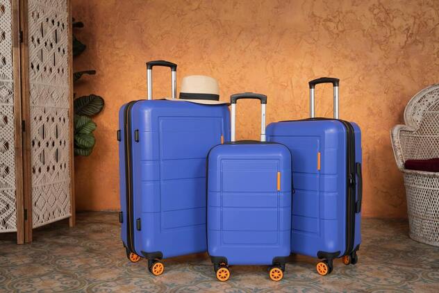 Conjunto de maletas de varios tamaños. 3 maletas de color azul, con detalles en los laterales y las ruedas de color naranja. La pared es de color ocre-naranja. | Cómo superar con éxito tu primer viaje en avión. | Equipaje y maletas, medidas y restricciones para viajar en avión. | Glutenacious Life.com